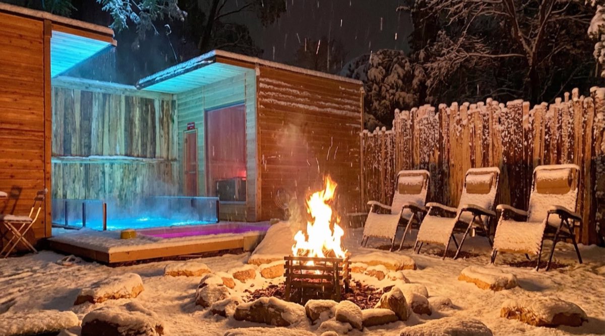 雪の夜、木々に包まれた森のサウナと焚き火
